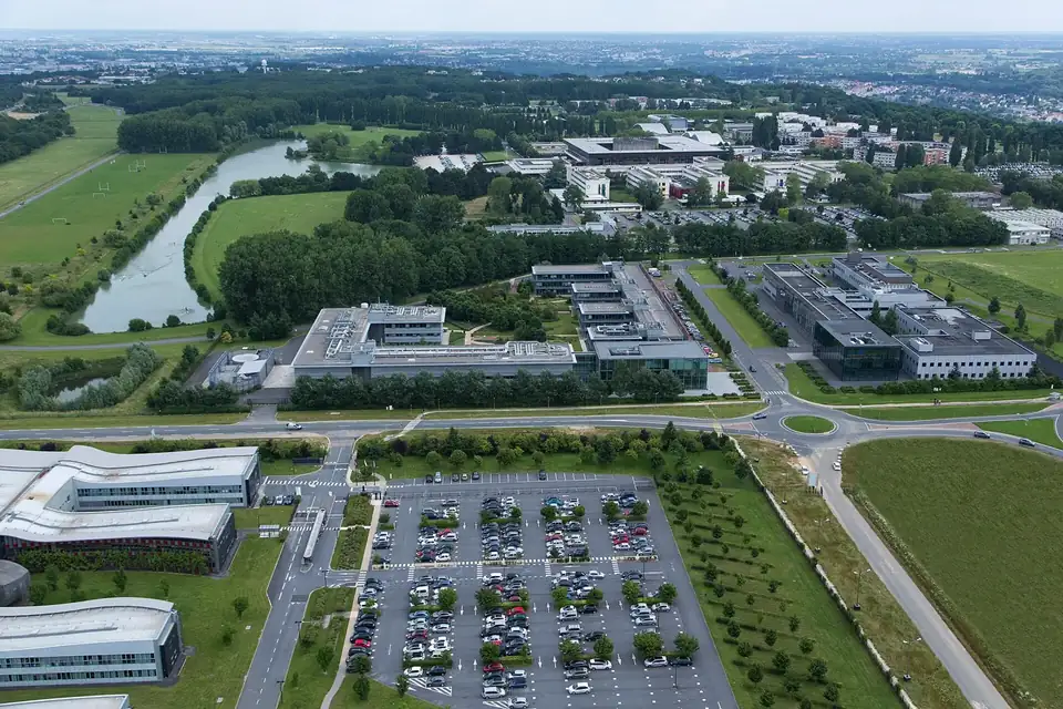 Vue aérienne d'un campus d'école d'ingénieurs avec ses bâtiments, un lac et des parkings, entouré de champs