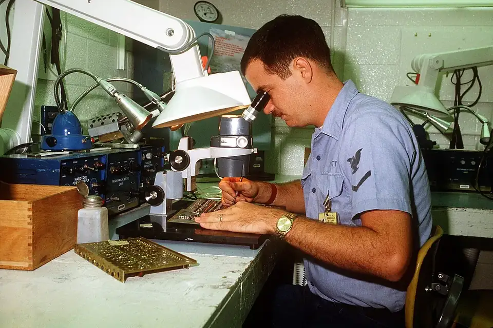 Un technicien examine une carte électronique à la loupe sur un établi de maintenance