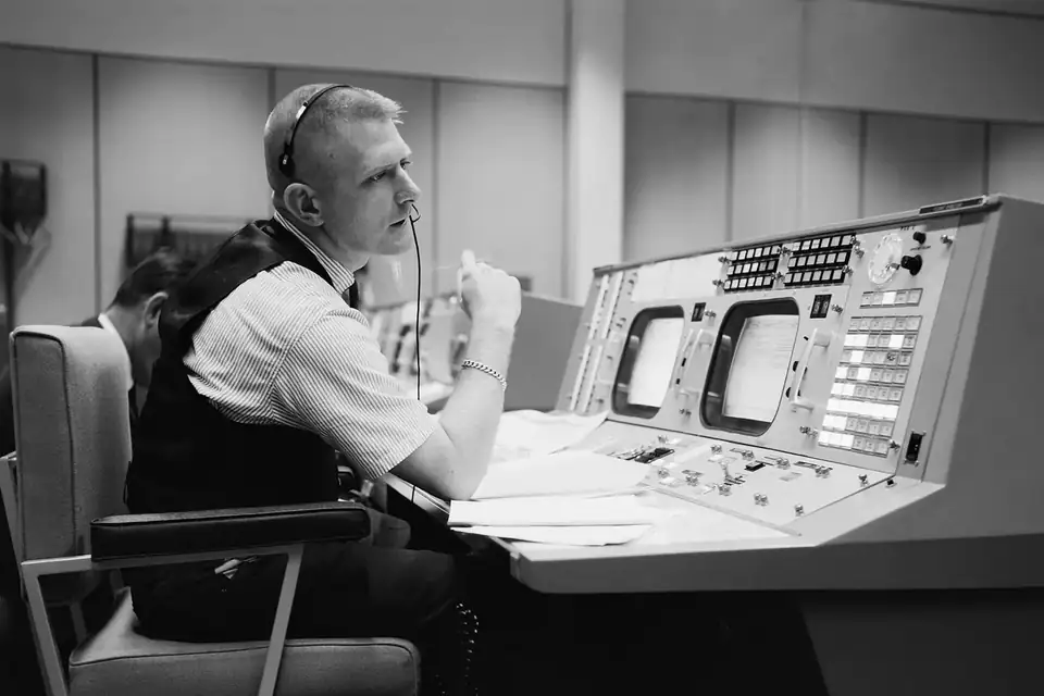 Un directeur de vol en chemise blanche, casque sur la tête, à sa console de contrôle dans les années 1960