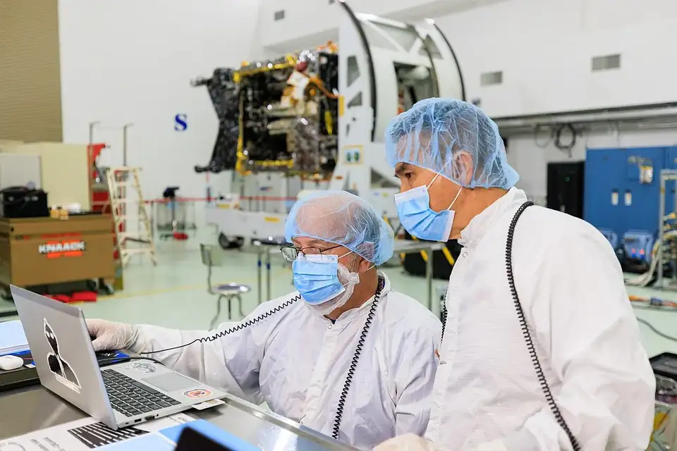 Une sonde spatiale couverte d'isolant doré et argenté, entourée de techniciens en salle blanche