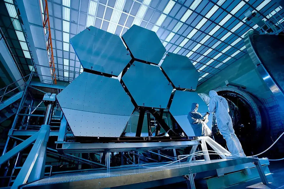 Des segments de miroir hexagonaux assemblés sur un banc d'essai, avec des techniciens en blouse