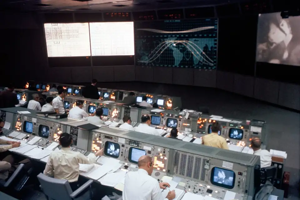 Une salle de contrôle des années 1960 avec des rangées de consoles et de grands écrans au mur