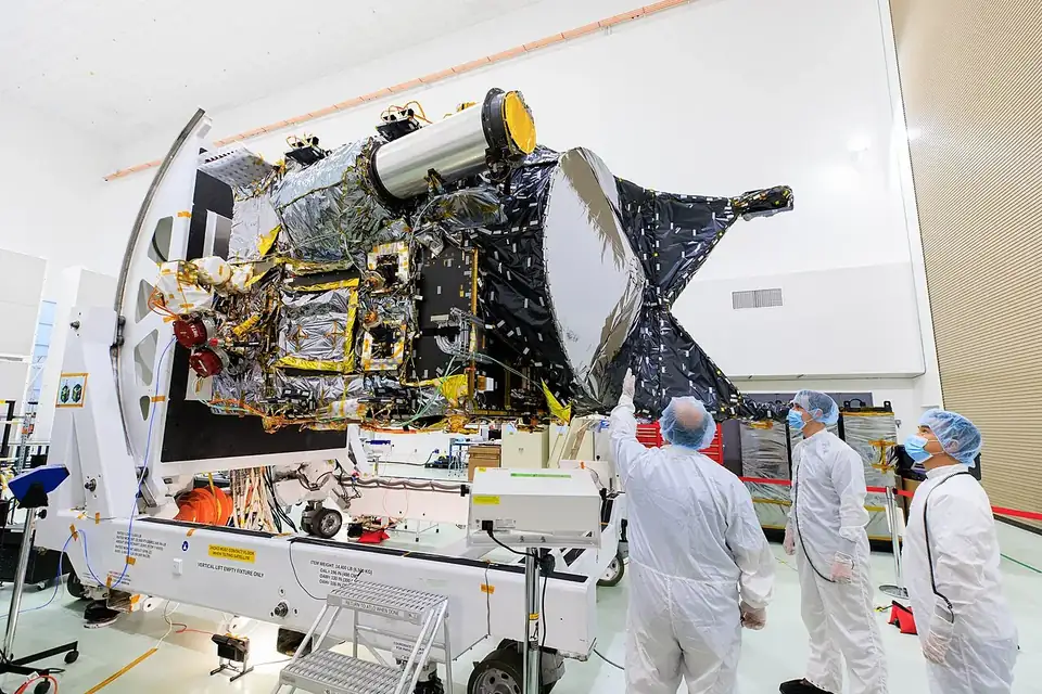 Des techniciens en combinaison de salle blanche autour d'une sonde spatiale en cours d'intégration