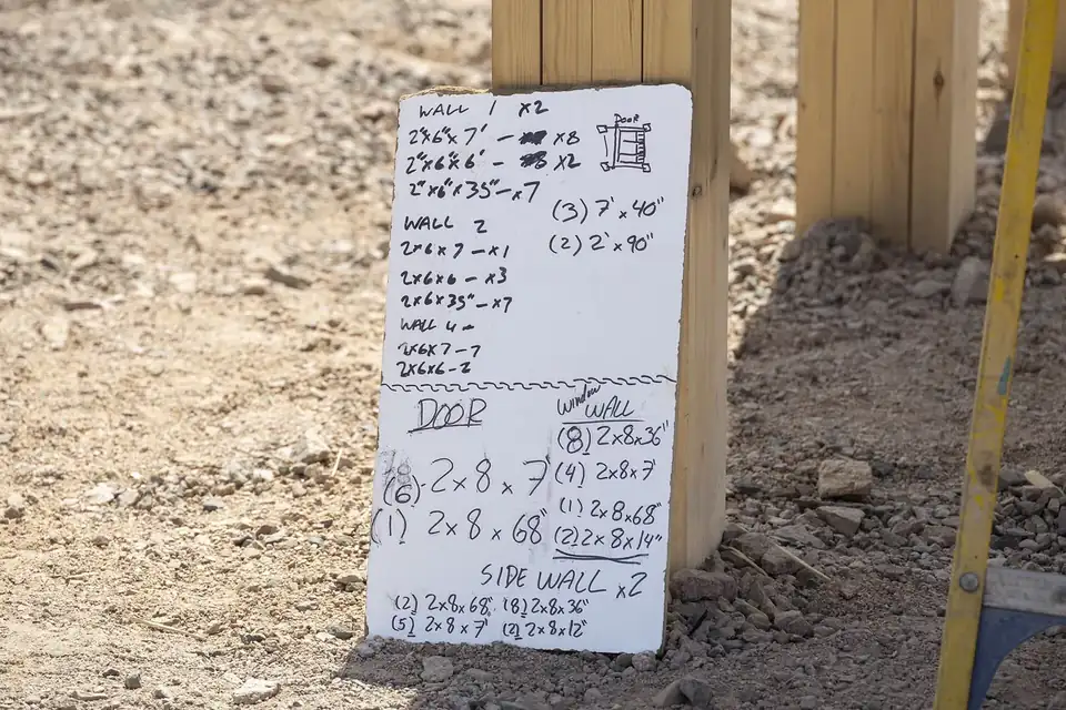 Un petit tableau blanc couvert de cotes et de calculs manuscrits, posé sur un chantier